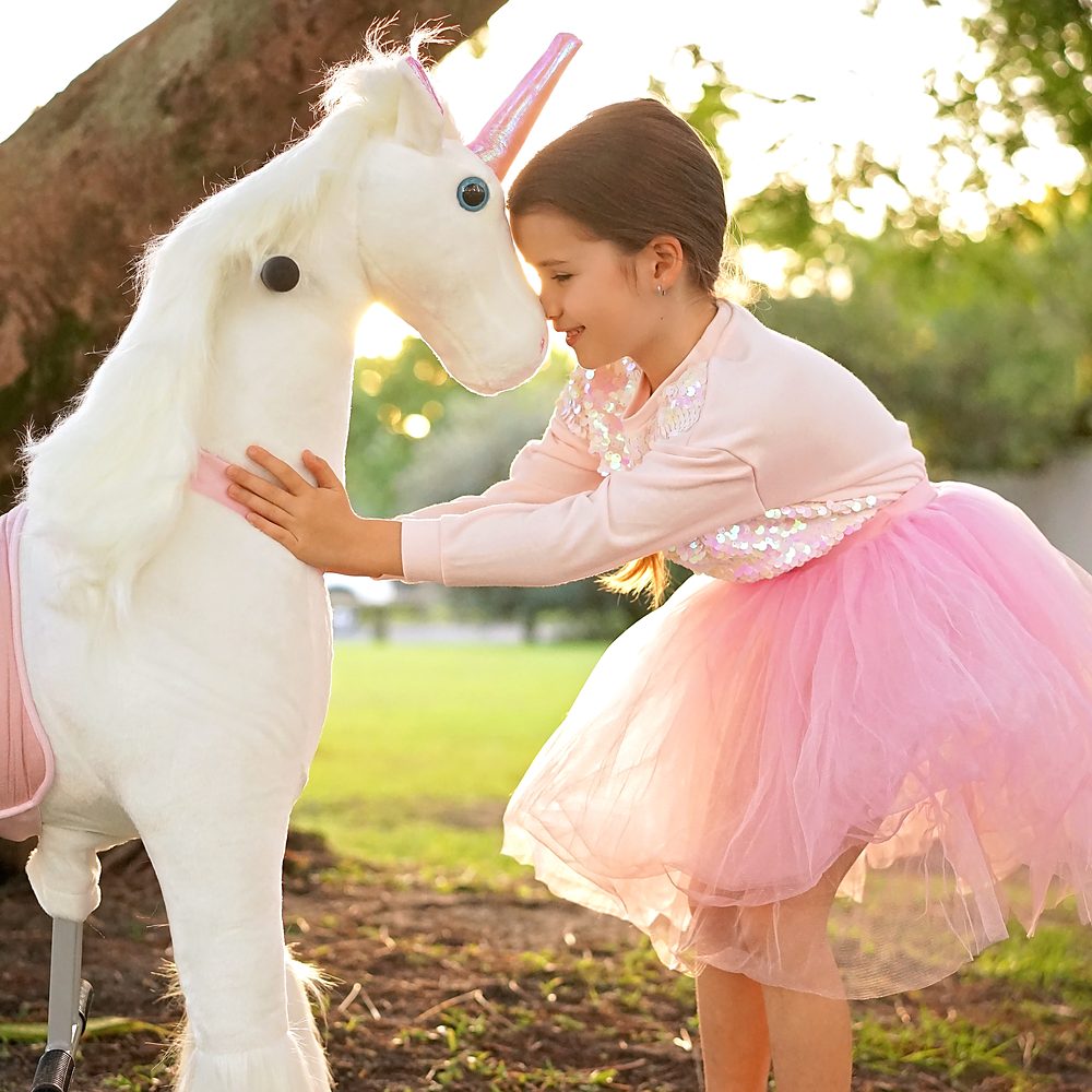 Little Riders pink and white unicorn ride-on toy - girl touching foreheads with her unicorn