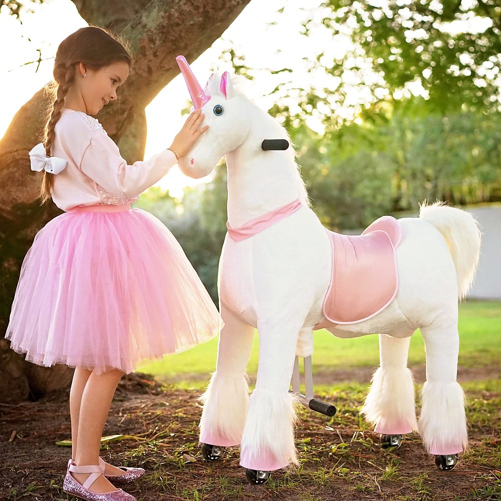 Little Riders pink and white unicorn ride-on toy - girl patting her pink and white unicorn at sunset