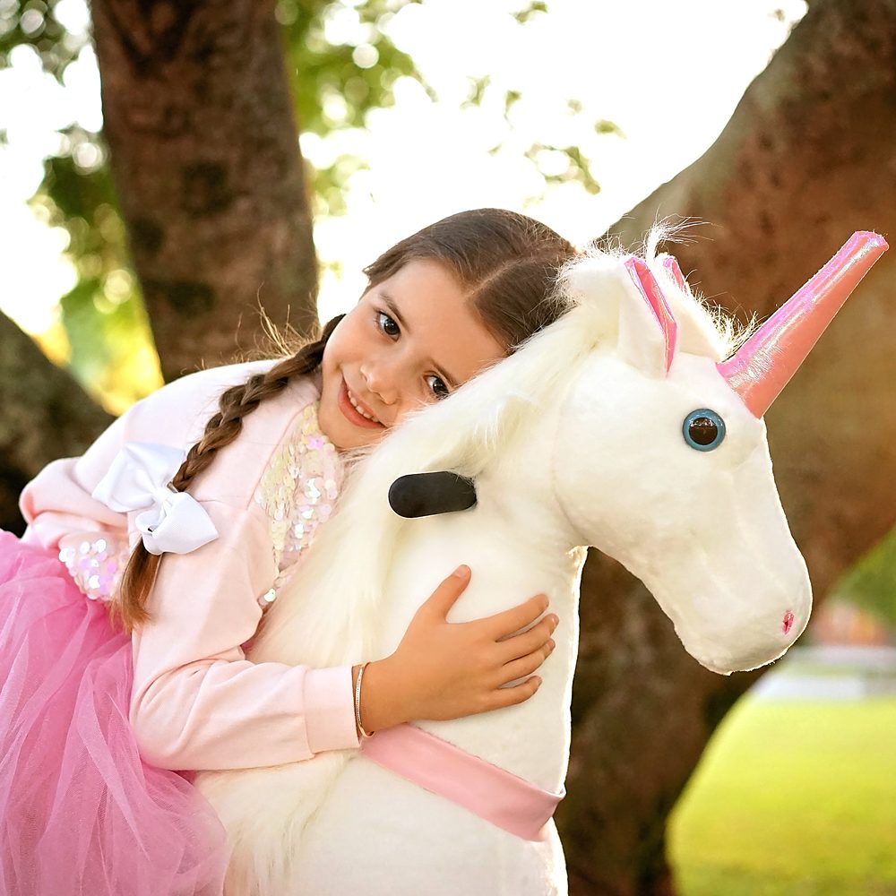 Little Riders pink and white unicorn ride-on toy - girl hugging her pink and white unicorn