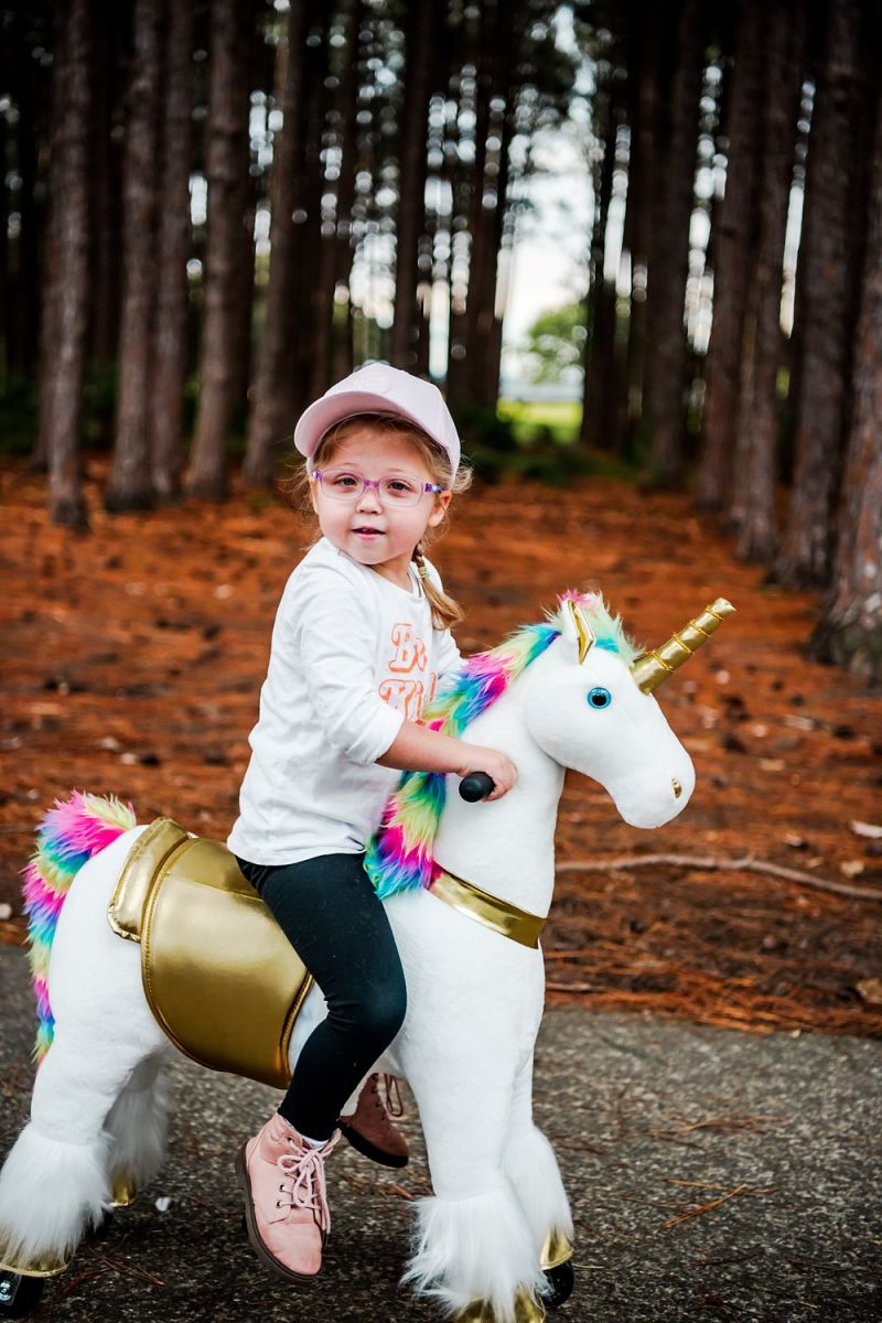 Little Riders rainbow unicorn ride-on toy - toddler riding her rainbow unicorn in the pine forest