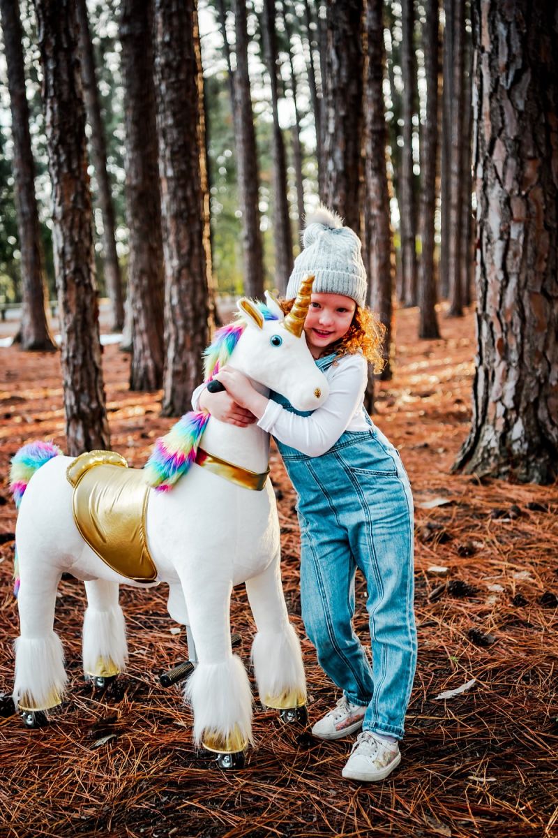 Little Riders rainbow unicorn ride-on toy - girl hugging her rainbow unicorn among the trees