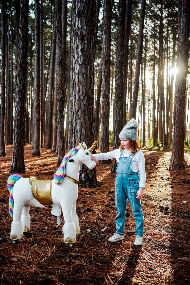 Little Riders rainbow unicorn ride-on toy - girl patting her rainbow unicorn in the forest
