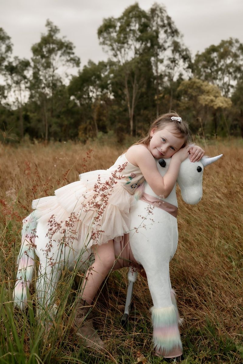 Little Riders unicorn ride-on toy - girl hugging her rainbow mane unicorn in the long grass