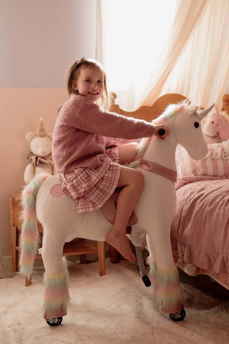 Little Riders unicorn ride-on toy - girl smiling while riding her unicorn in her bedroom