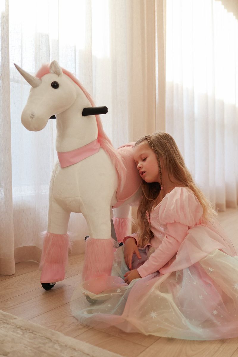 Little Riders pink unicorn ride-on toy - girl resting against her pink unicorn by the window